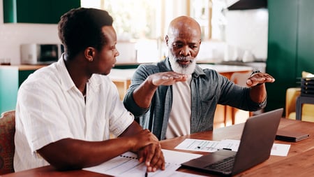 Two men discussing finances in front of a laptop. 