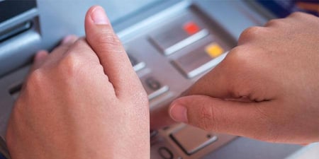 Close up of someone using their hand to hide the pin pad while entering their PIN at an ATM