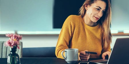 A woman at her kitchen table looking at her computer screen