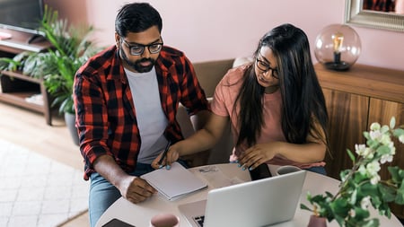 A couple sitting down while looking over a laptop.
