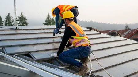 two workers on a house fixing a roof. 