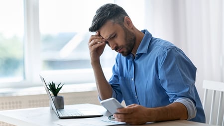A man sitting in front of a laptop with his hand covering his forehead. 