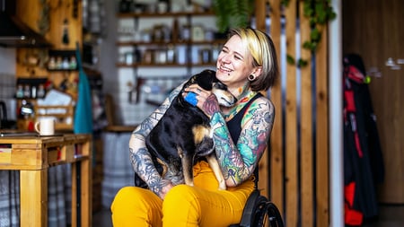 A tattooed women petting a dog that is in her lap. 