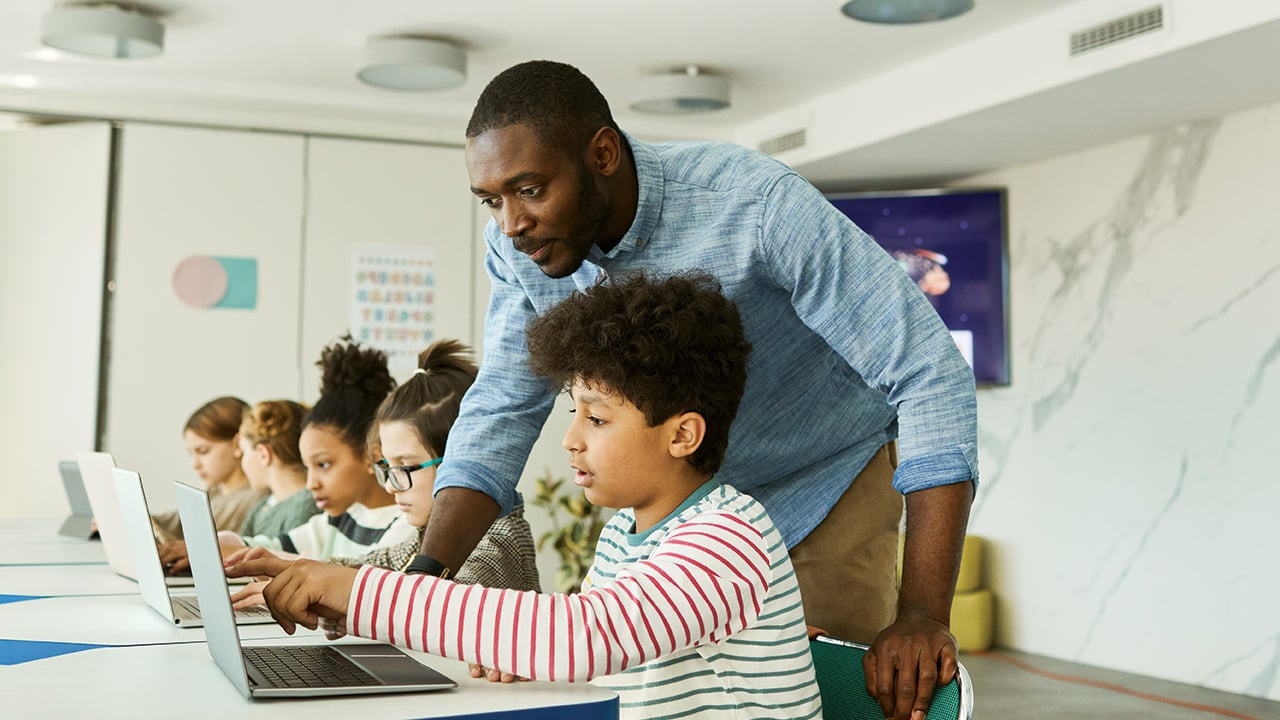 A teacher and a student pointing to something on a laptop