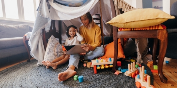 A parent reading to their child under a home fort. 